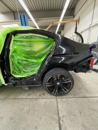Schwarzes Auto mit grünem Schutzmaterial am offenen Türbereich in einer Werkstatt.