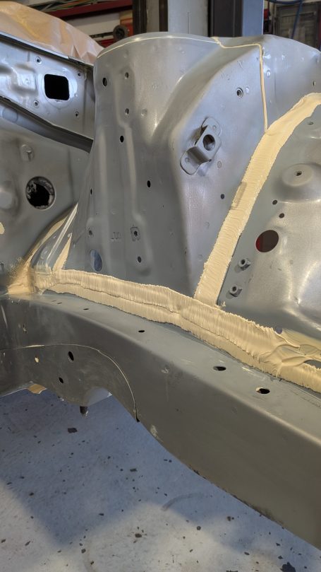 Grau lackierter Fahrzeugrahmen mit Spachtelmasse und sichtbaren Bohrlöchern.