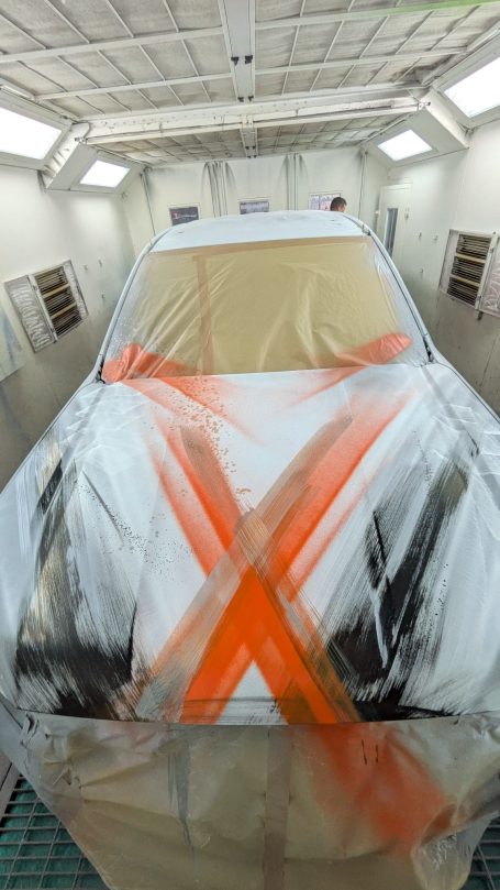 Ein Auto, das zum Lackieren in einer Sprühkabine abgedeckt ist, mit orangefarbenen Markierungen.