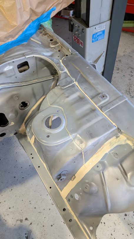 Eine Metalloberfläche mit gelben Abklebestreifen und einem blauen Tuch im Hintergrund.