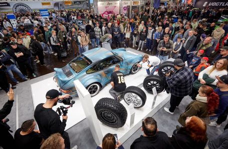 Blaues Auto umgeben von Menschen auf einer Messe, mit Reifen im Vordergrund.