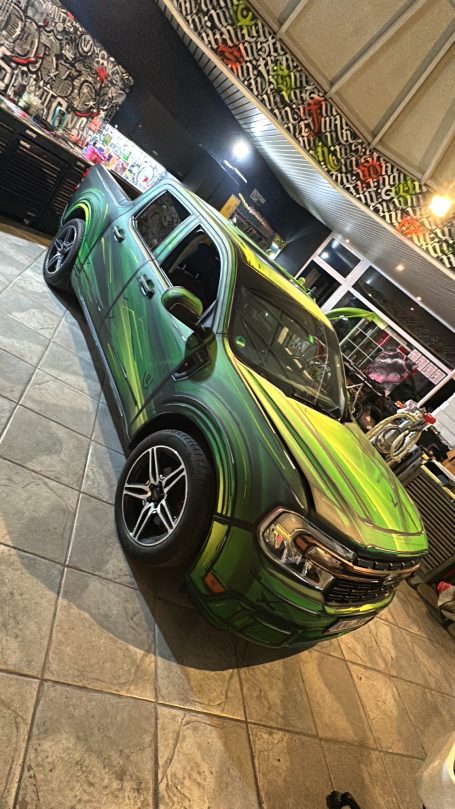 Ein modifiziertes Auto mit grünem und schwarzem Lack steht in einer Halle.