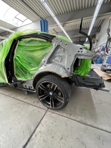 BMW-Auto mit grünem Schutz auf unvollständiger Karosserie in einer Werkstatt.