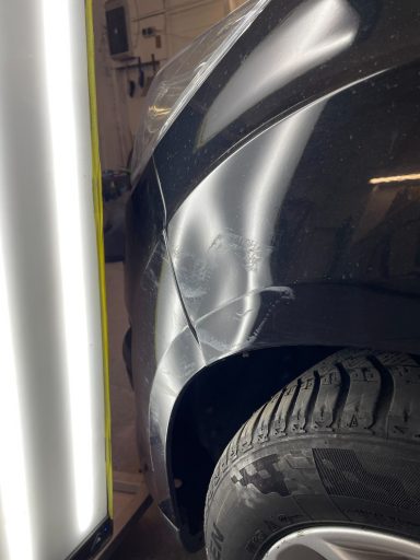 Delle an der hinteren Stoßstange eines schwarzen Fahrzeugs, Reifen sichtbar.